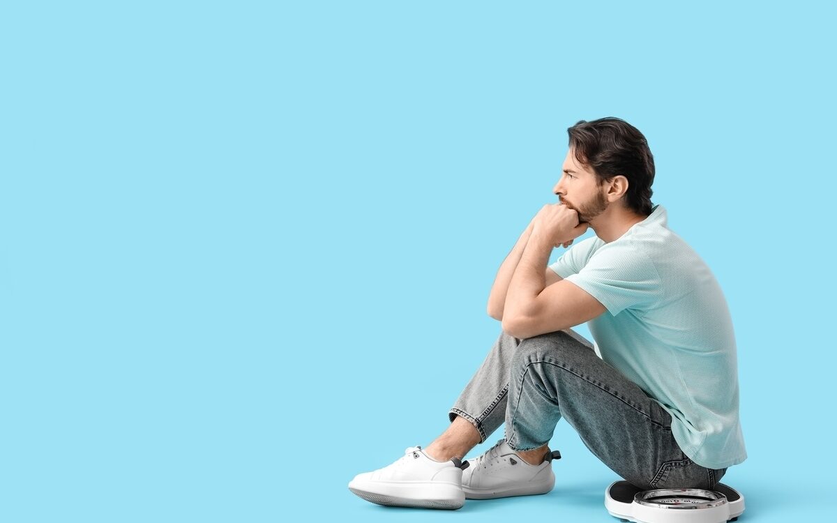 Can Weight Loss Treatments Help When Diet and Exercise Fail? 1 Man sitting on a scale feeling frustrated with a weight loss plateau considering medical weight loss treatments